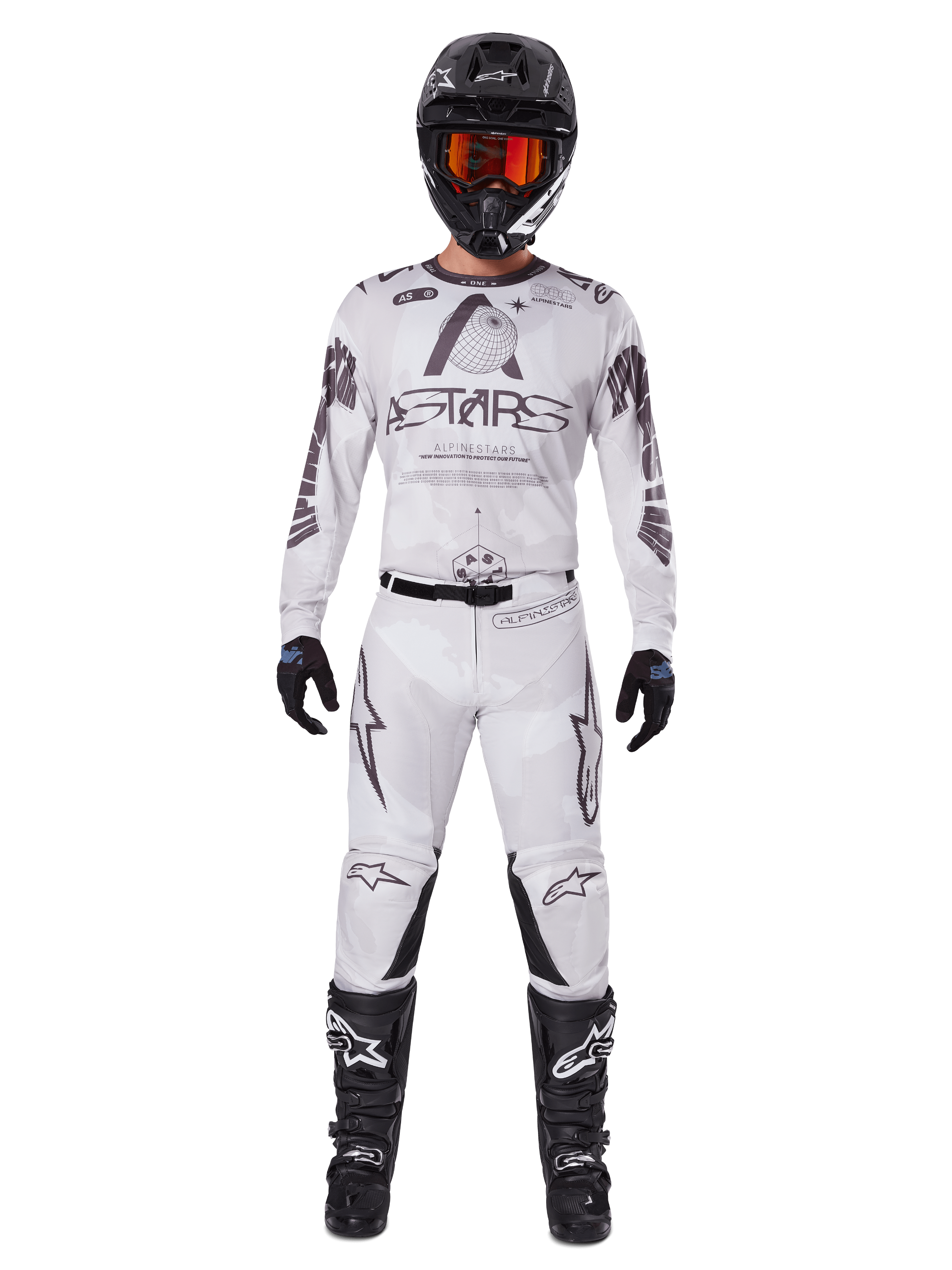 Pilota di motocross con pantaloni Alpinestars 2025 Racer Hollow in Light Camo Brown, maglia a maniche lunghe coordinata bianca e grigia, casco nero con occhiali arancione-rossi, guanti e stivali neri, completo da gara per prestazioni off-road