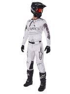Alpinestars 2025 Racer Hollow Pants, pantaloni da motocross, Light Camo Brown, mostrati come parte di un kit completo da gara con maglia bianca, casco nero e stivali neri, con pannelli neri rinforzati sulle ginocchia e un design mimetico discreto.