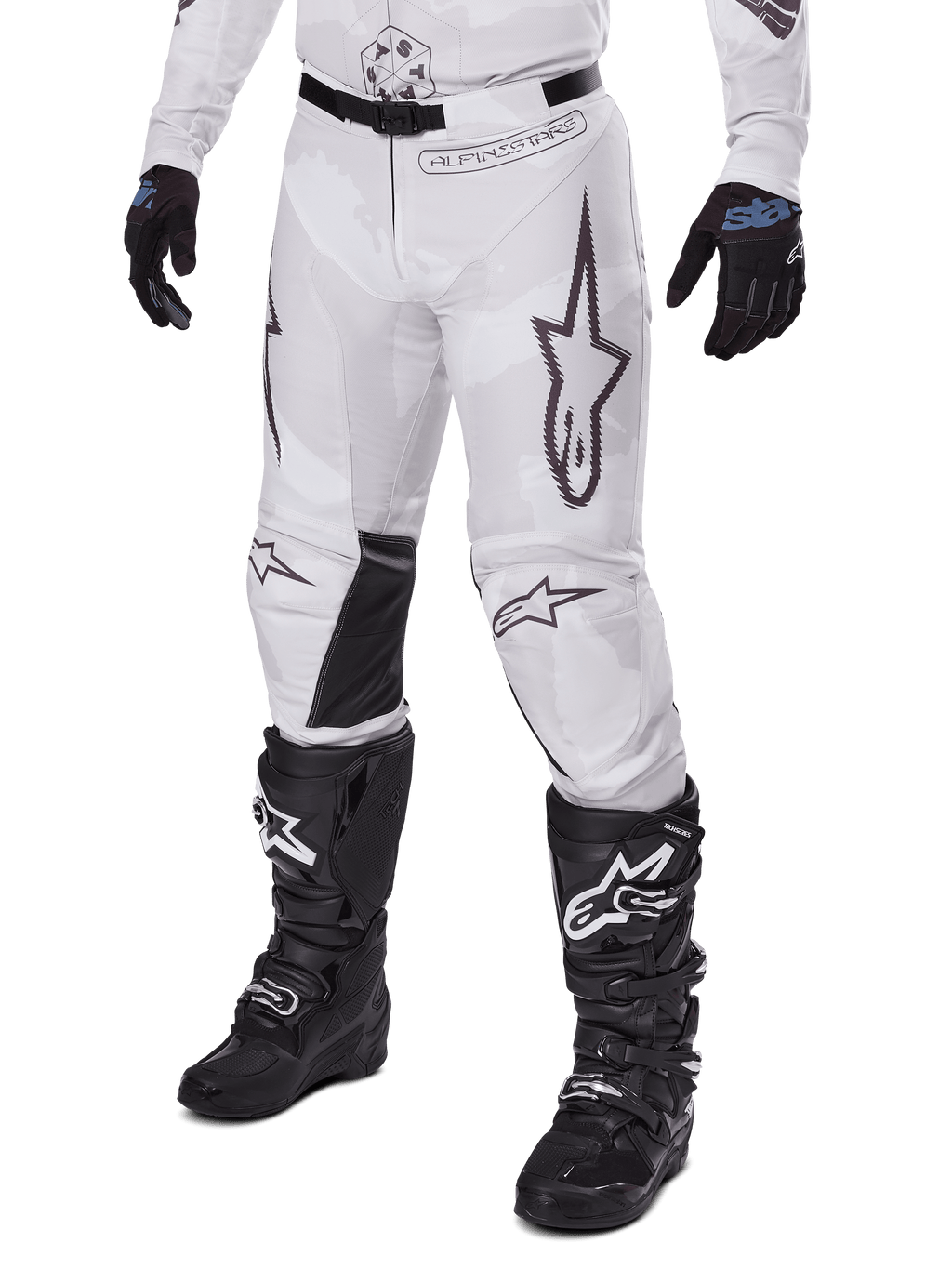 Pantaloni Alpinestars Racer Hollow 2025, pantaloni da motocross, camo bianco e grigio, con grandi loghi a stella profilati in nero e pannelli interni alle ginocchia in pelle nera, indossati con stivali e guanti da motocross neri, design resistente per corse fuoristrada.