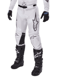 Pantaloni Alpinestars Racer Hollow 2025, pantaloni da motocross, camo bianco e grigio, con grandi loghi a stella profilati in nero e pannelli interni alle ginocchia in pelle nera, indossati con stivali e guanti da motocross neri, design resistente per corse fuoristrada.