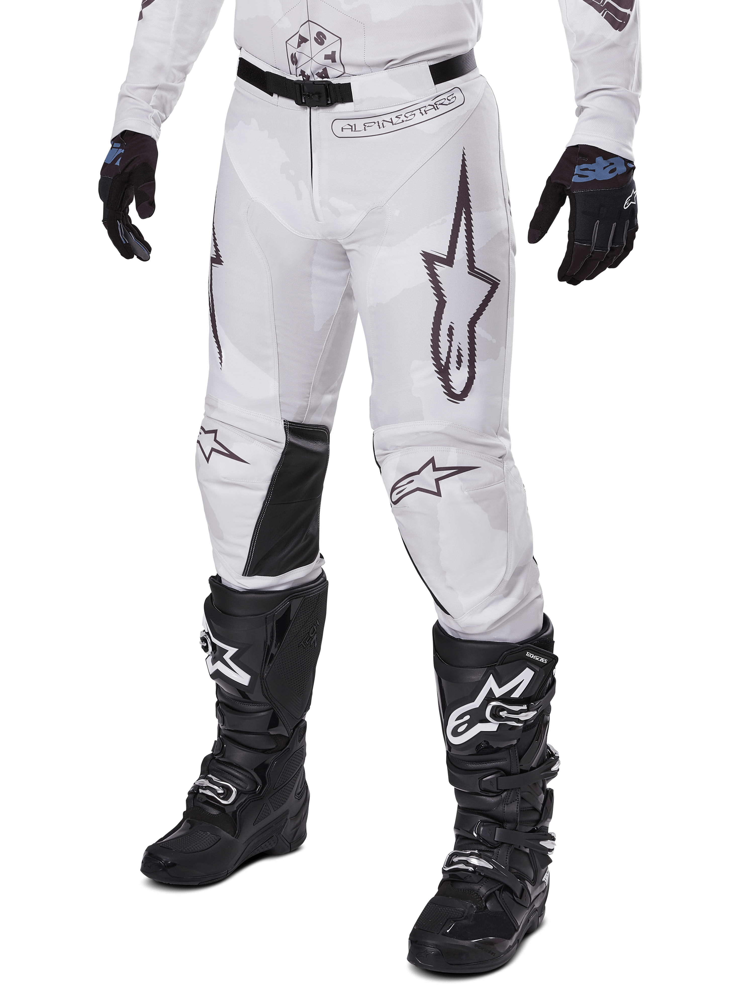 Pantaloni Alpinestars Racer Hollow 2025, pantaloni da motocross, camo bianco e grigio, con grandi loghi a stella profilati in nero e pannelli interni alle ginocchia in pelle nera, indossati con stivali e guanti da motocross neri, design resistente per corse fuoristrada.