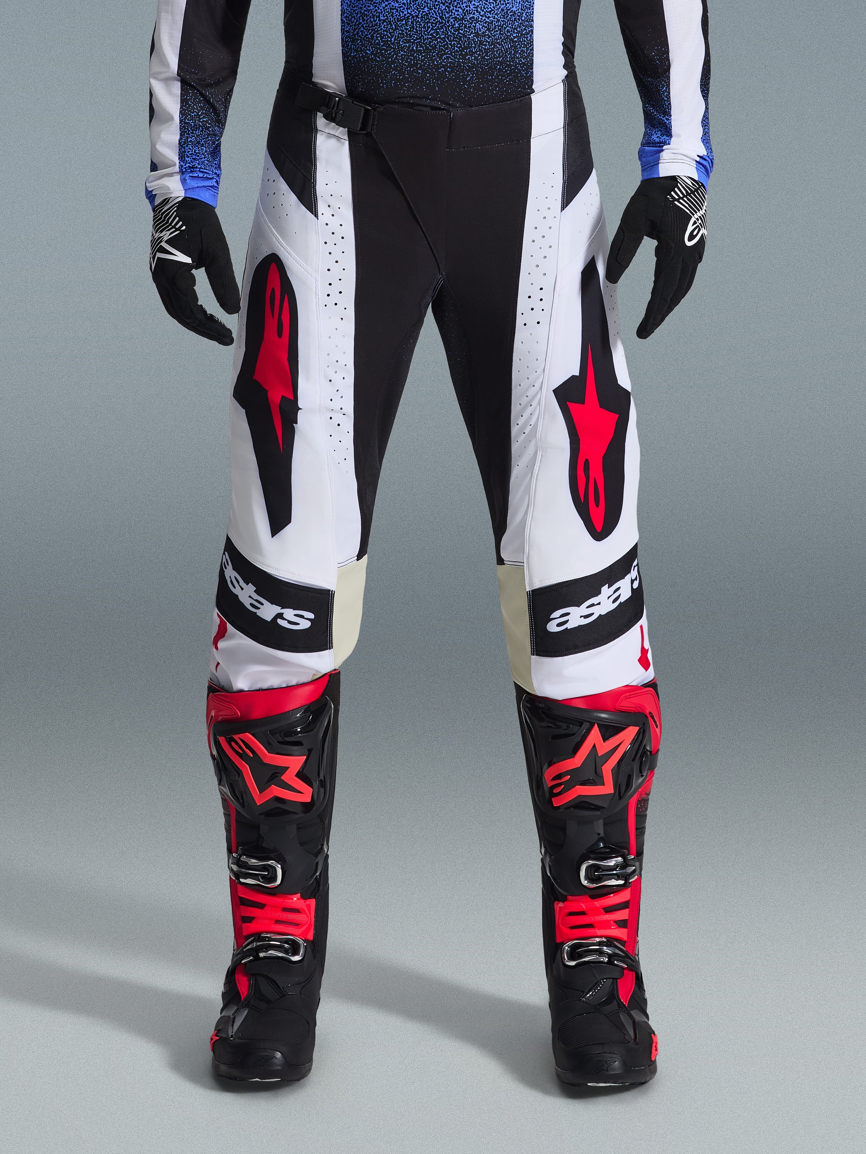 Alpinestars 2026 Techstar Knif Pants, pantaloni da motocross, nero, bianco e rosso, indossati con stivali rossi e neri coordinati e guanti neri, con vistosi loghi a stella rossi su pannelli bianchi e dettagli tecnici traforati per gare off-road.