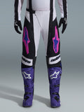 Alpinestars 2026 Techstar Knif Pants, pantaloni da motocross, nero, bianco e viola con accenti rosa e blu, indossati con stivali da gara viola e guanti neri, con taglio ergonomico da gara e grafiche con logo audaci per prestazioni fuoristrada