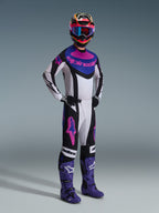 Pilota di motocross con il set completo Alpinestars Techstar Knif 2026, maglia bianca con dettagli neri, blu e rosa, pantaloni coordinati con loghi Astars rosa, casco multicolore con occhiali, stivali da gara viola, abbigliamento tecnico ad alte prestazioni per motocross