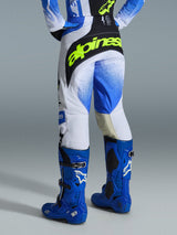 Alpinestars 2026 Techstar Knif Pants, pantaloni da motocross, blu UCLA, nero e giallo fluo, vista posteriore con logo Alpinestars giallo neon sul retro, base bianca con grafiche blu sfumate, indossati con stivali da motocross blu brillante