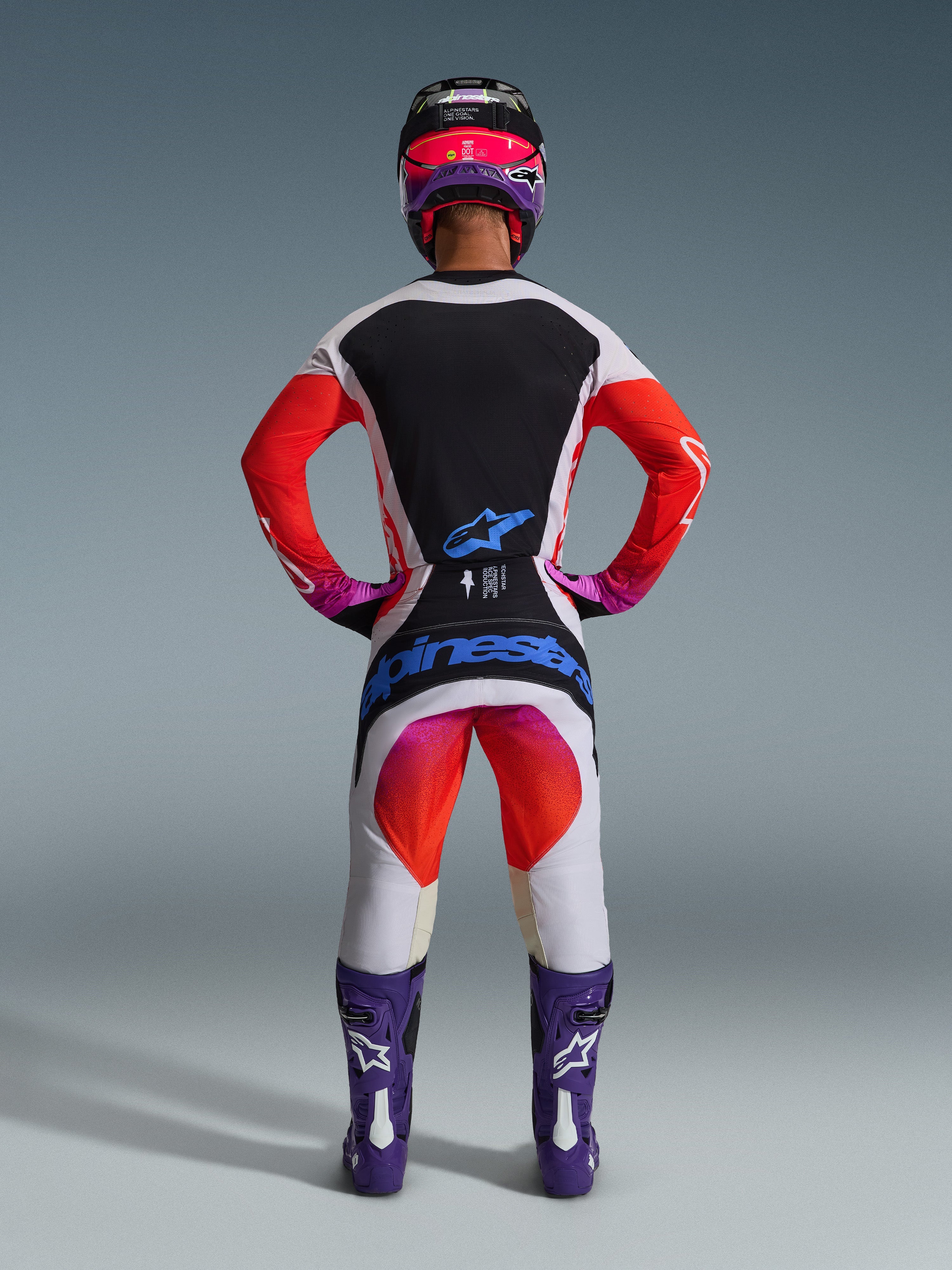 Set completo Alpinestars 2026 Techstar Knif, abbigliamento completo da motocross visto da dietro, maglia bianca e nera con maniche a sfumatura rossa, pantaloni bianchi con accenti rossi e rosa, coordinato con stivali viola e casco rosa, branding blu audace, kit professionale per corse fuoristrada
