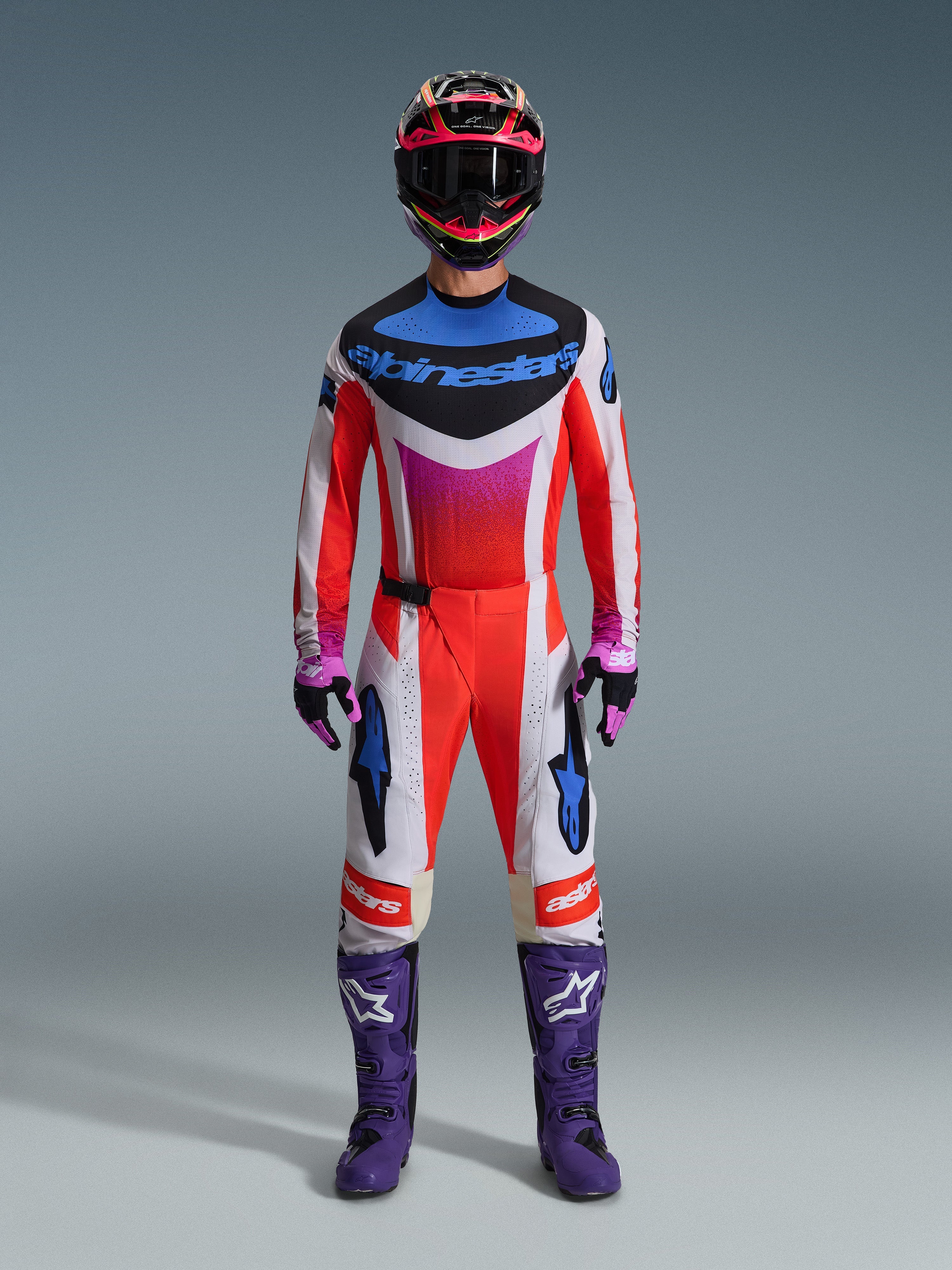 Pilota di motocross con il set Alpinestars 2026 Techstar Knif, completo da gara rosso, bianco e nero con loghi blu e accenti rosa, stivali viola con loghi bianchi, guanti rosa e neri e casco nero e rosa, attrezzatura professionale da competizione fuoristrada