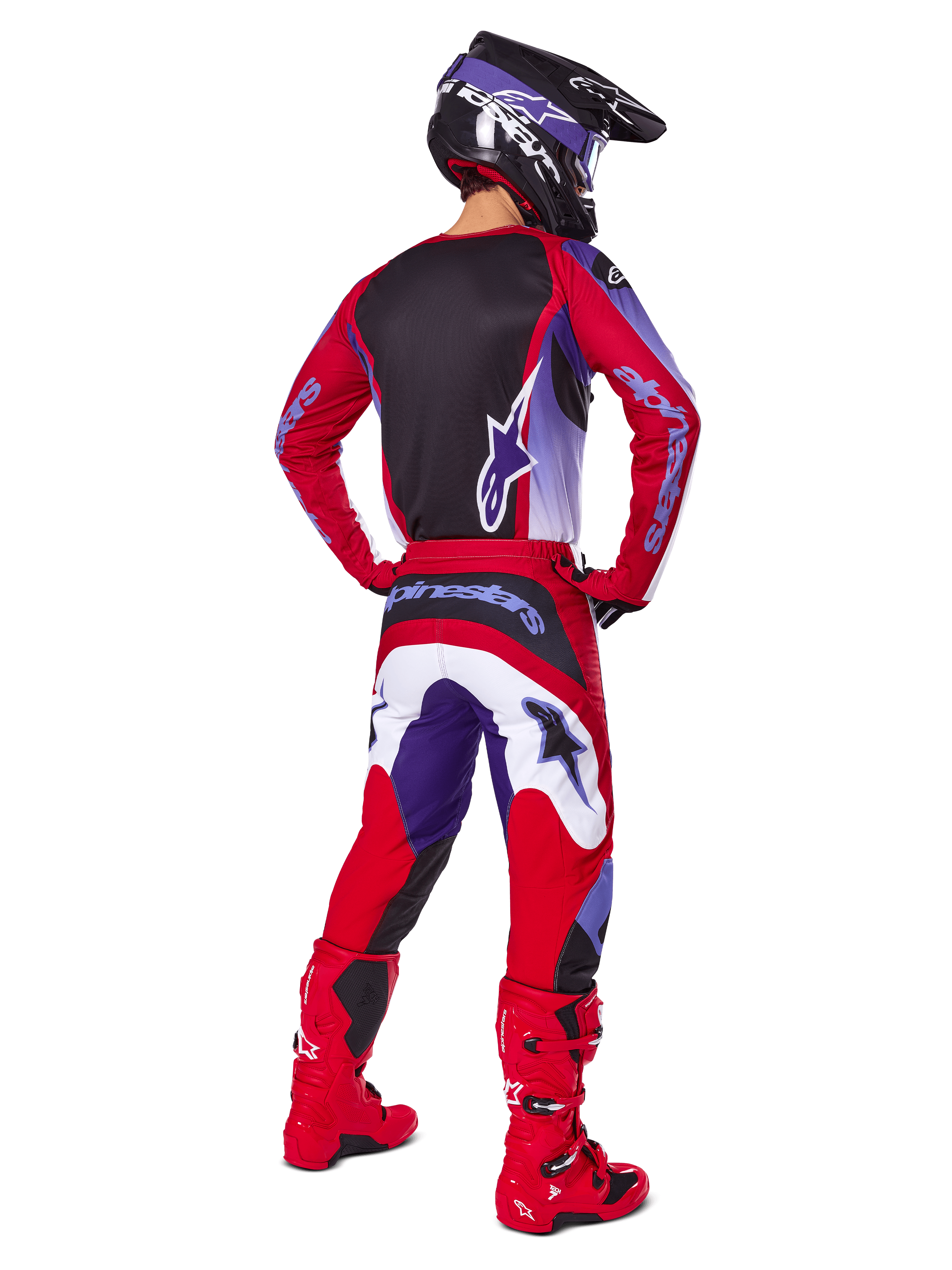Pilota di motocross visto da dietro che indossa pantaloni Alpinestars Fluid Wurx 2025, viola e rosso brillante con accenti bianchi e neri, maglia coordinata, casco nero e stivali rossi, completo coordinato per corse fuoristrada
