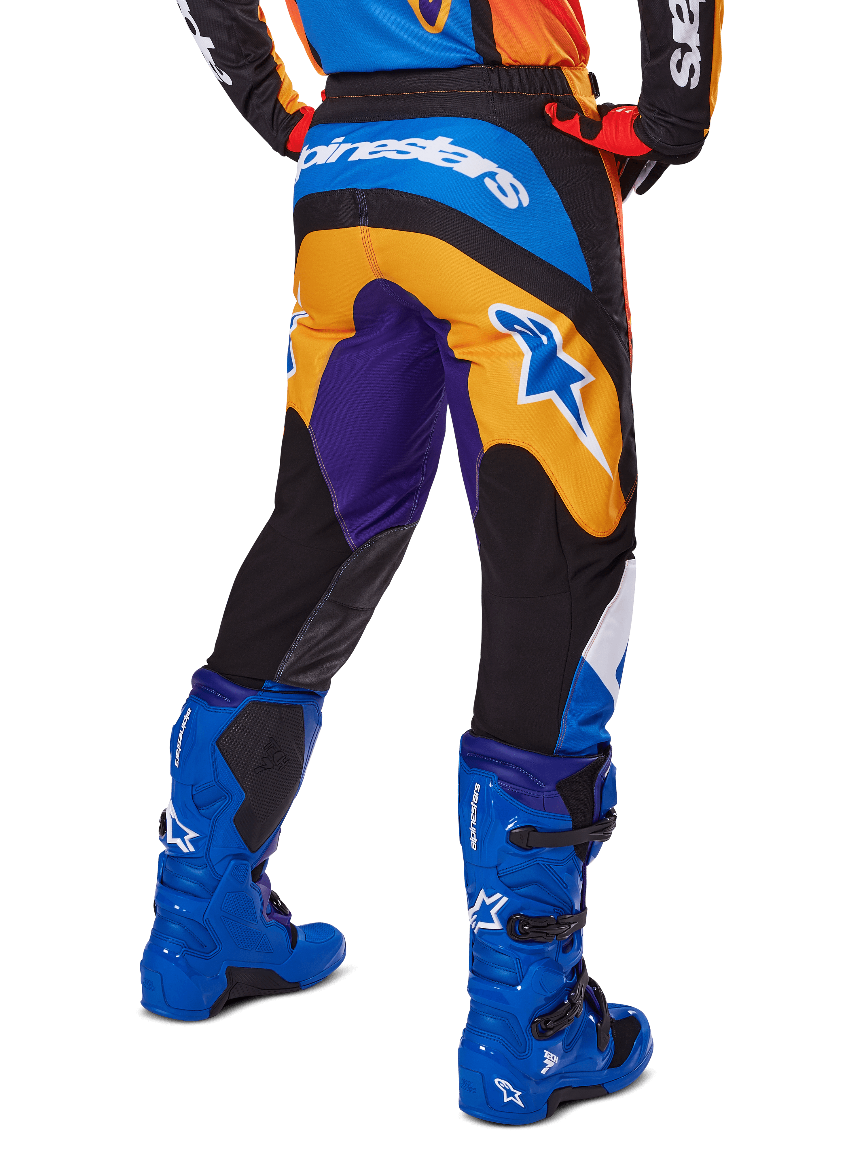 Alpinestars pantaloni Fluid Wurx 2025, pantaloni da motocross, multicolore con arancione, viola e blu, vista posteriore che mostra il logo Alpinestars bianco sul retro, abbinati a stivali da motocross blu, vestibilità atletica per gare off-road