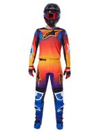 Alpinestars Pantaloni Fluid Wurx 2025, pantaloni da motocross, sfumatura multicolore arancione, giallo e viola, indossati con maglia coordinata, casco nero con occhiali blu, guanti rossi e neri e stivali blu, abbigliamento da gara motocross coordinato