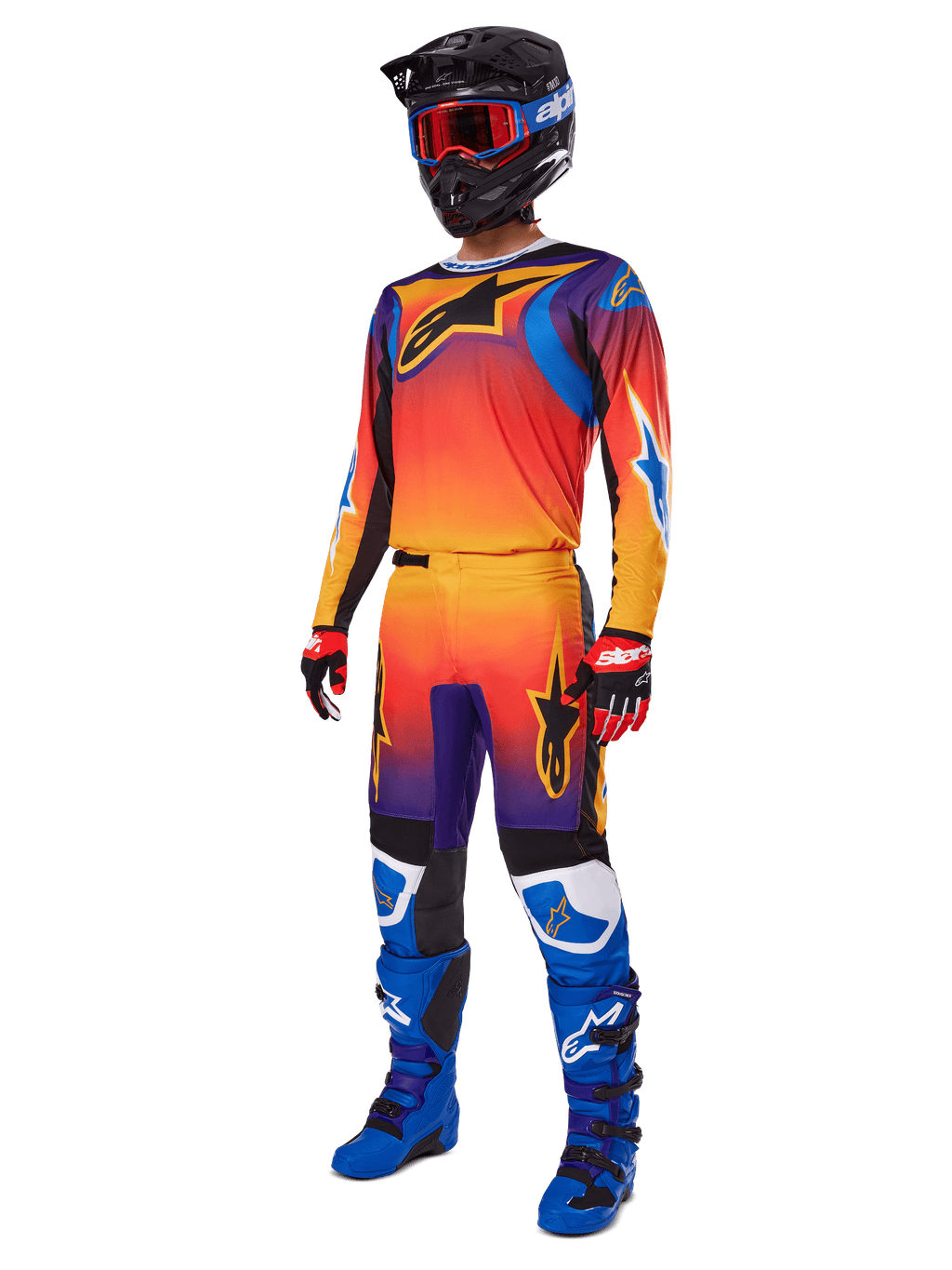 Pilota di motocross con abbigliamento da gara completo, pantaloni Alpinestars 2025 Fluid Wurx e maglia coordinata con sfumatura multicolore arancione, rossa e viola, casco nero con occhiali rossi, stivali blu e neri, guanti rossi e neri, outfit coordinato per corse fuoristrada