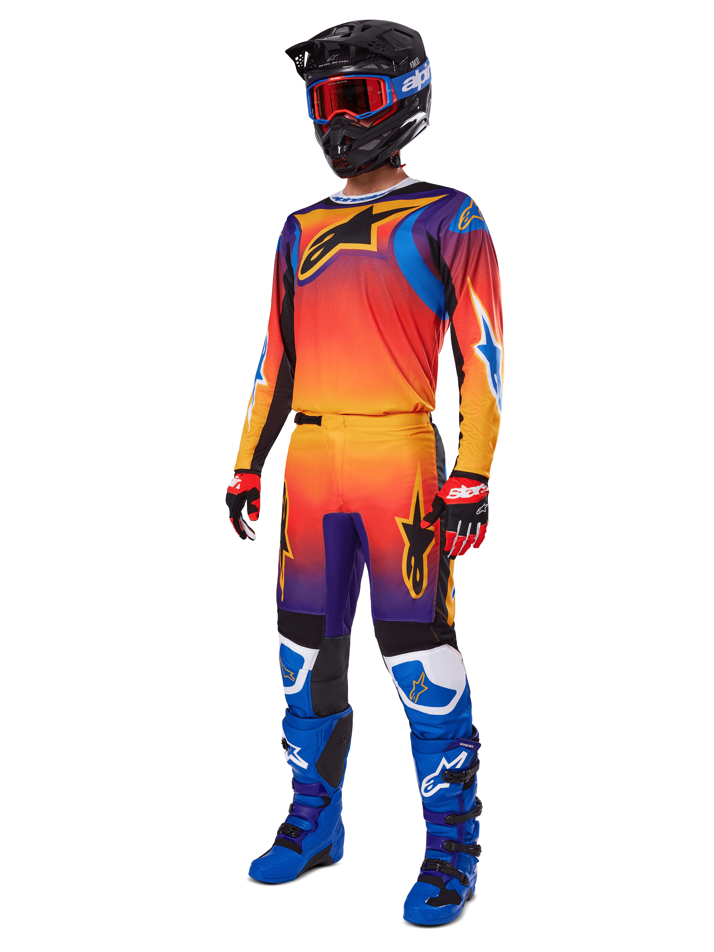 Pilota di motocross con abbigliamento da gara completo, pantaloni Alpinestars 2025 Fluid Wurx e maglia coordinata con sfumatura multicolore arancione, rossa e viola, casco nero con occhiali rossi, stivali blu e neri, guanti rossi e neri, outfit coordinato per corse fuoristrada