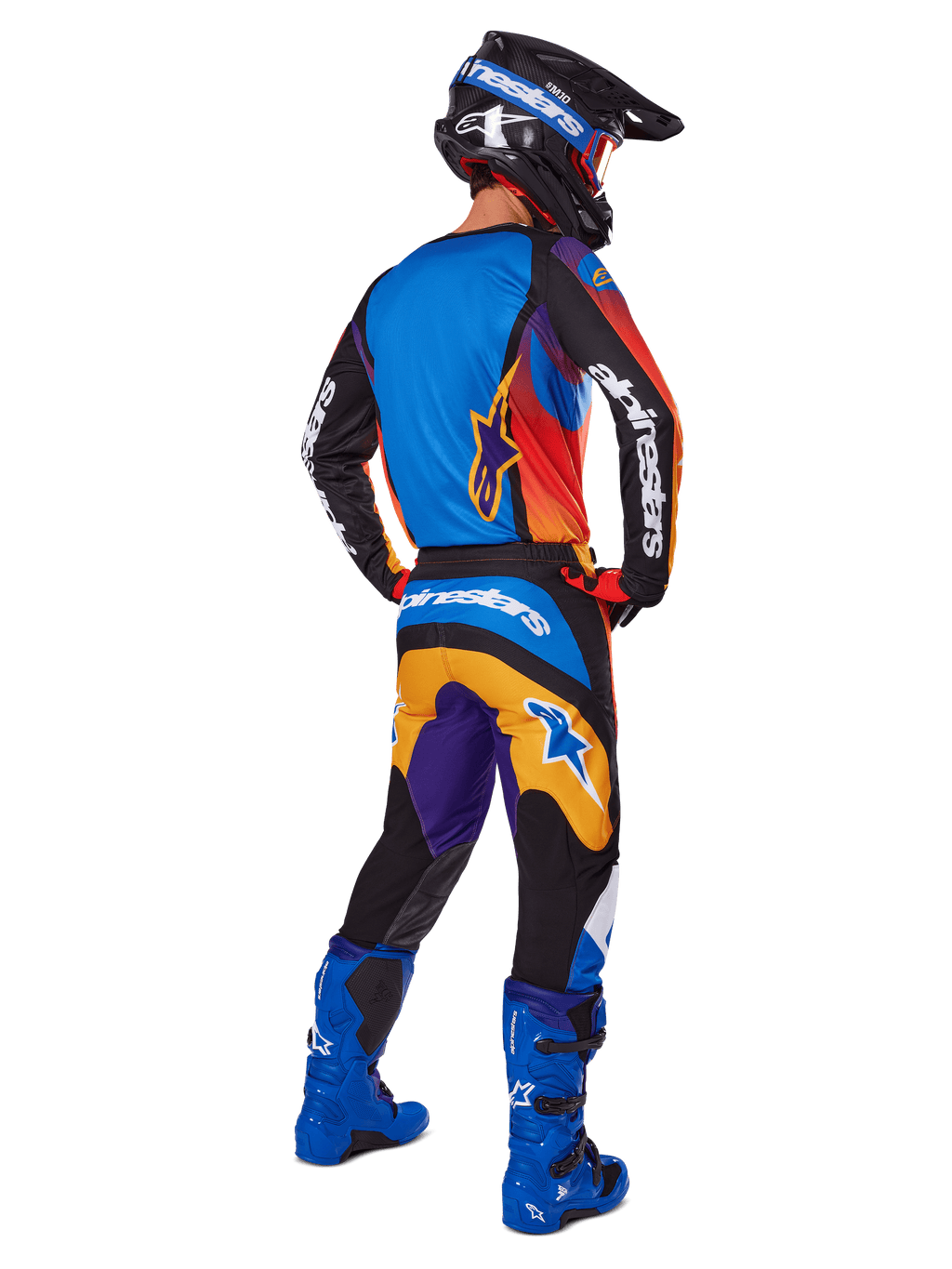 Pilota di motocross visto da dietro con pantaloni Alpinestars 2025 Fluid Wurx, design multicolore con dettagli blu, arancioni, gialli e viola, maglia abbinata, stivali blu acceso e casco nero, equipaggiamento completo per fuoristrada