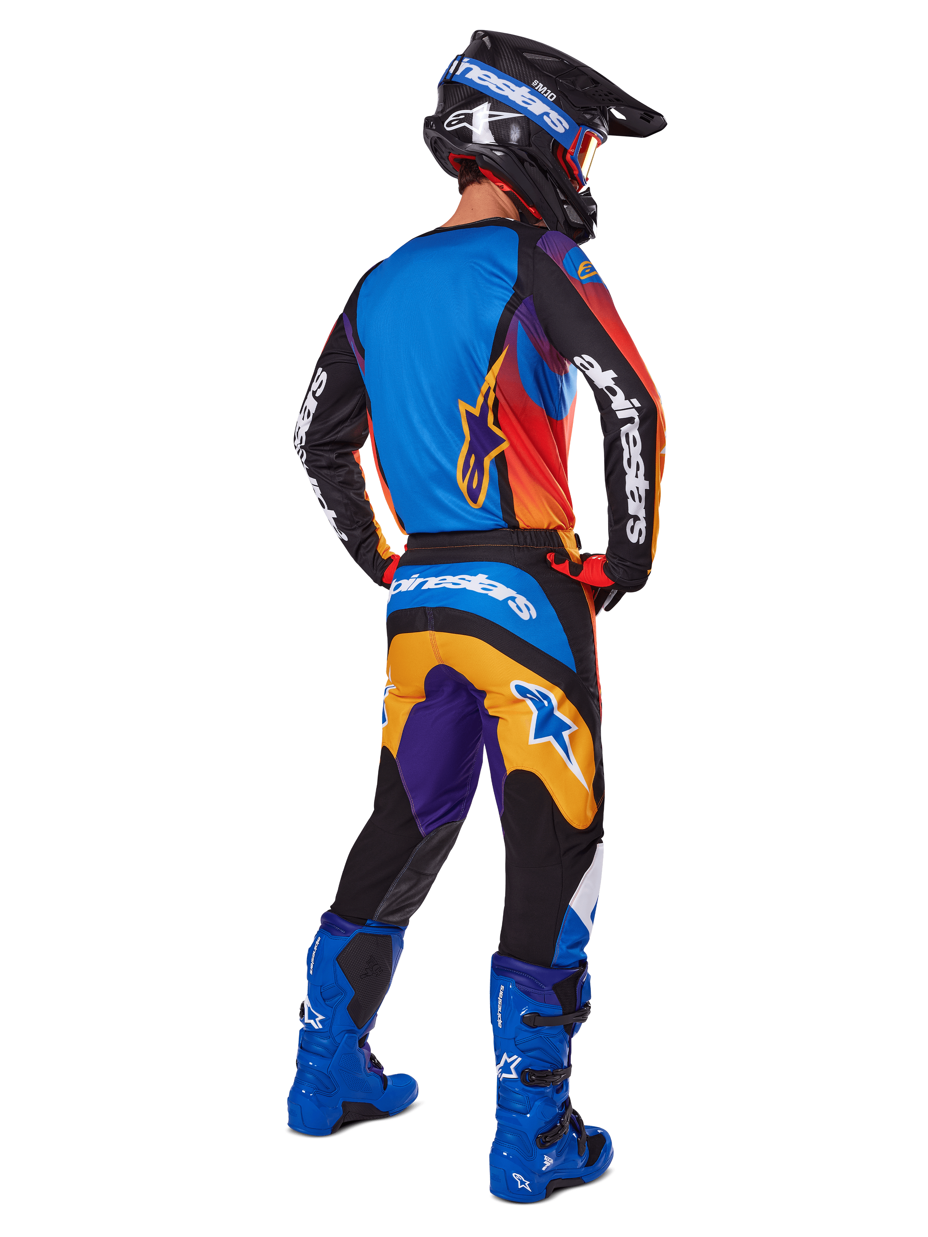 Pilota di motocross visto da dietro con pantaloni Alpinestars 2025 Fluid Wurx, design multicolore con dettagli blu, arancioni, gialli e viola, maglia abbinata, stivali blu acceso e casco nero, equipaggiamento completo per fuoristrada