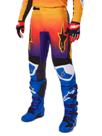 Alpinestars 2025 Fluid Wurx Pants, pantaloni da motocross, sfumatura multicolore arancione, rossa e viola con pannelli neri e blu, indossati con stivali blu e guanti rossi, con grafica del logo a stella e dettagli bianchi sulle ginocchia, abbigliamento tecnico resistente per fuoristrada