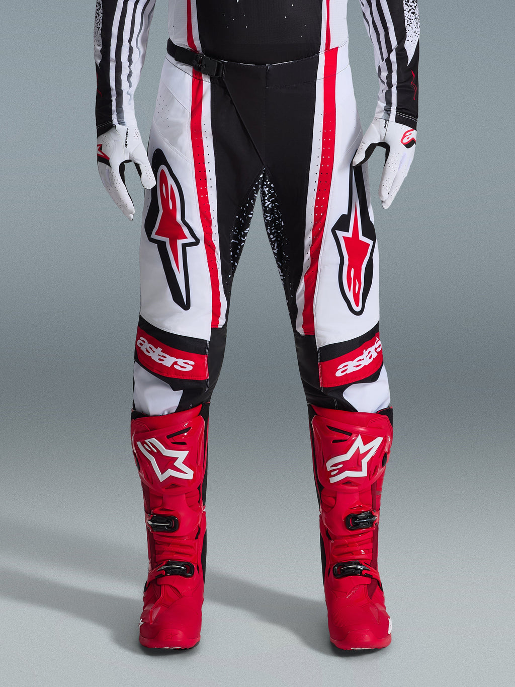 Alpinestars pantaloni Techstar Nomur 2026, pantaloni da motocross, nero, bianco e rosso, indossati con stivali rossi e guanti bianchi, con audaci loghi rossi sulle cosce e marchio 'astars' sulle ginocchia, design racing multi-pannello per prestazioni off-road