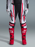 Alpinestars pantaloni Techstar Nomur 2026, pantaloni da motocross, nero, bianco e rosso, indossati con stivali rossi e guanti bianchi, con audaci loghi rossi sulle cosce e marchio 'astars' sulle ginocchia, design racing multi-pannello per prestazioni off-road