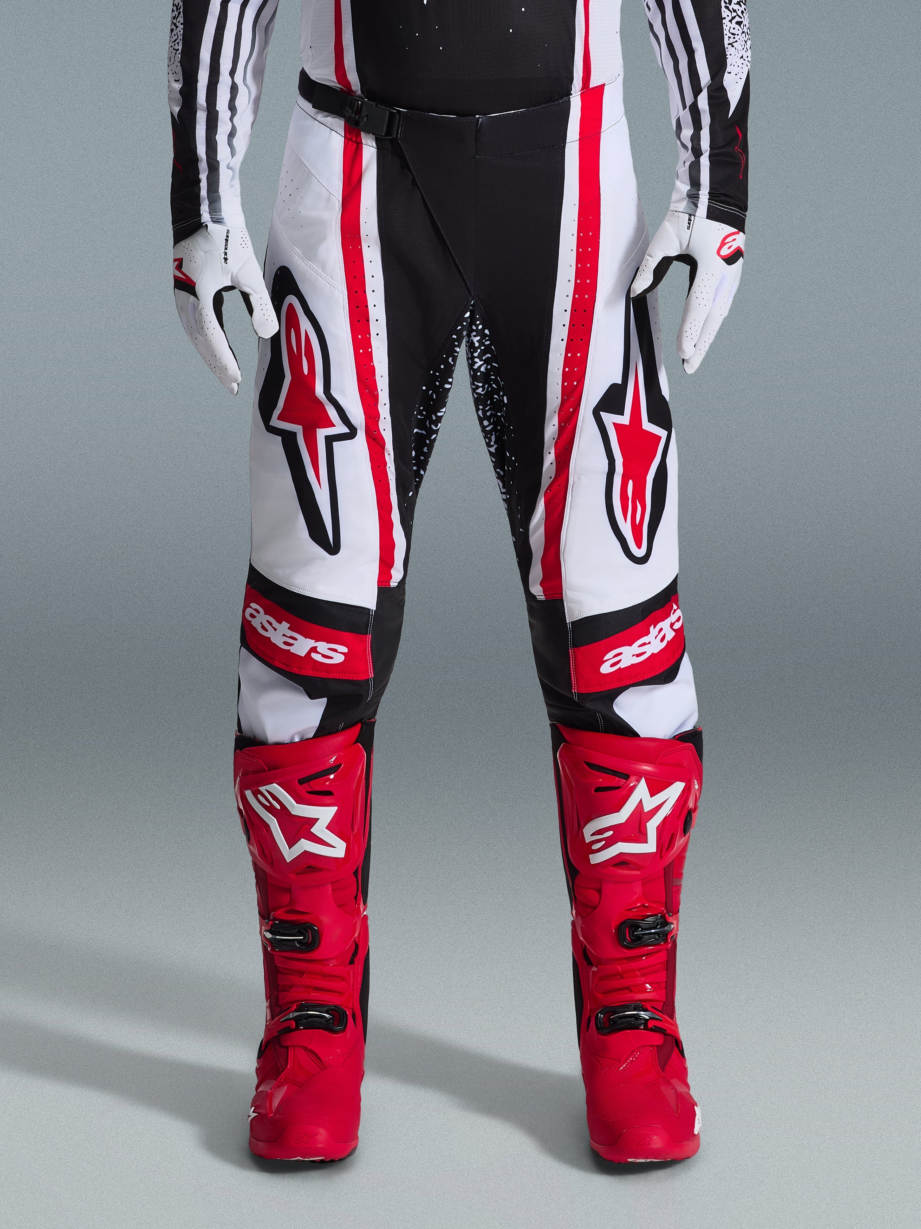 Alpinestars pantaloni Techstar Nomur 2026, pantaloni da motocross, nero, bianco e rosso, indossati con stivali rossi e guanti bianchi, con audaci loghi rossi sulle cosce e marchio 'astars' sulle ginocchia, design racing multi-pannello per prestazioni off-road