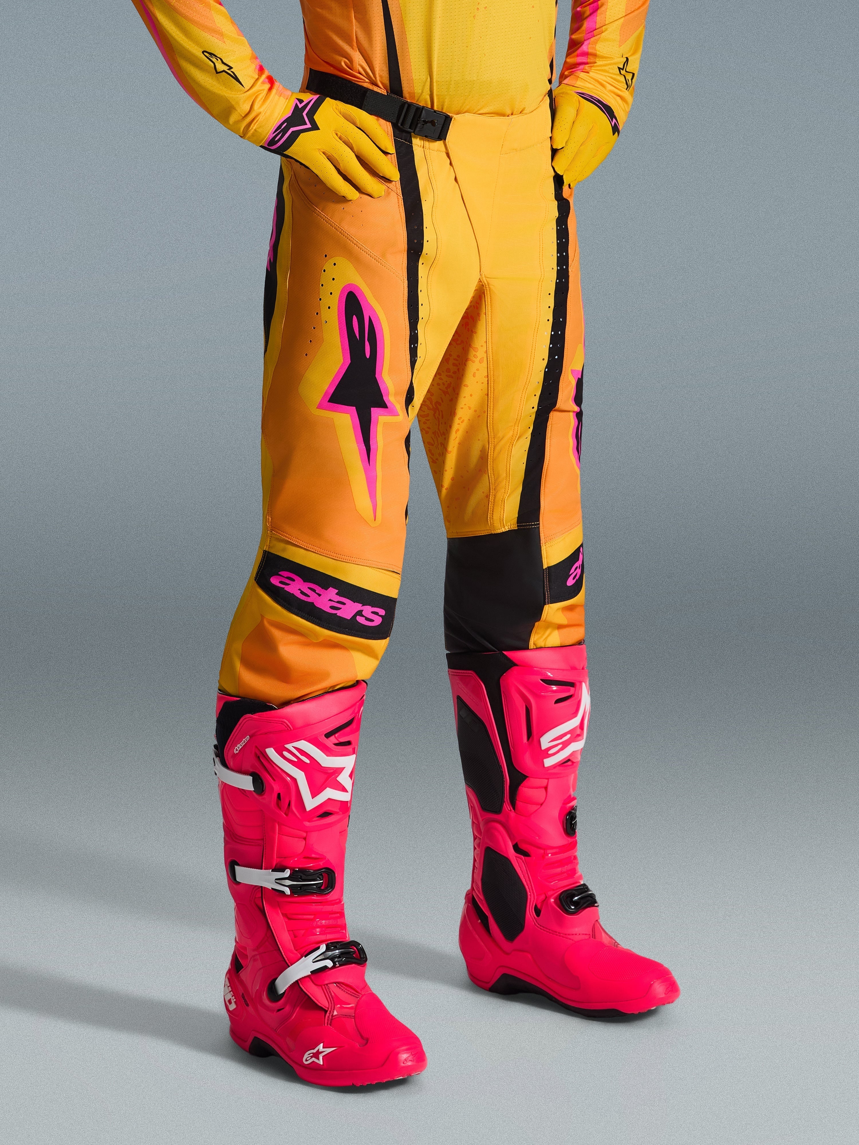 Alpinestars 2026 Techstar Nomur Pants, pantaloni da motocross, arancione, giallo e rosa, indossati con maglia e guanti gialli coordinati e stivali rosa acceso, vestibilità atletica con loghi rosa e fibbia magnetica nera, abbigliamento vivace per competizioni off-road