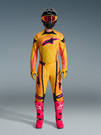 Pilota di motocross con set completo Alpinestars Techstar Nomur 2026, maglia e pantaloni arancioni, gialli e rosa, guanti coordinati gialli e rosa, stivali da corsa rosa acceso e casco nero con occhiali rosa, abbigliamento da motocross coordinato ad alte prestazioni.