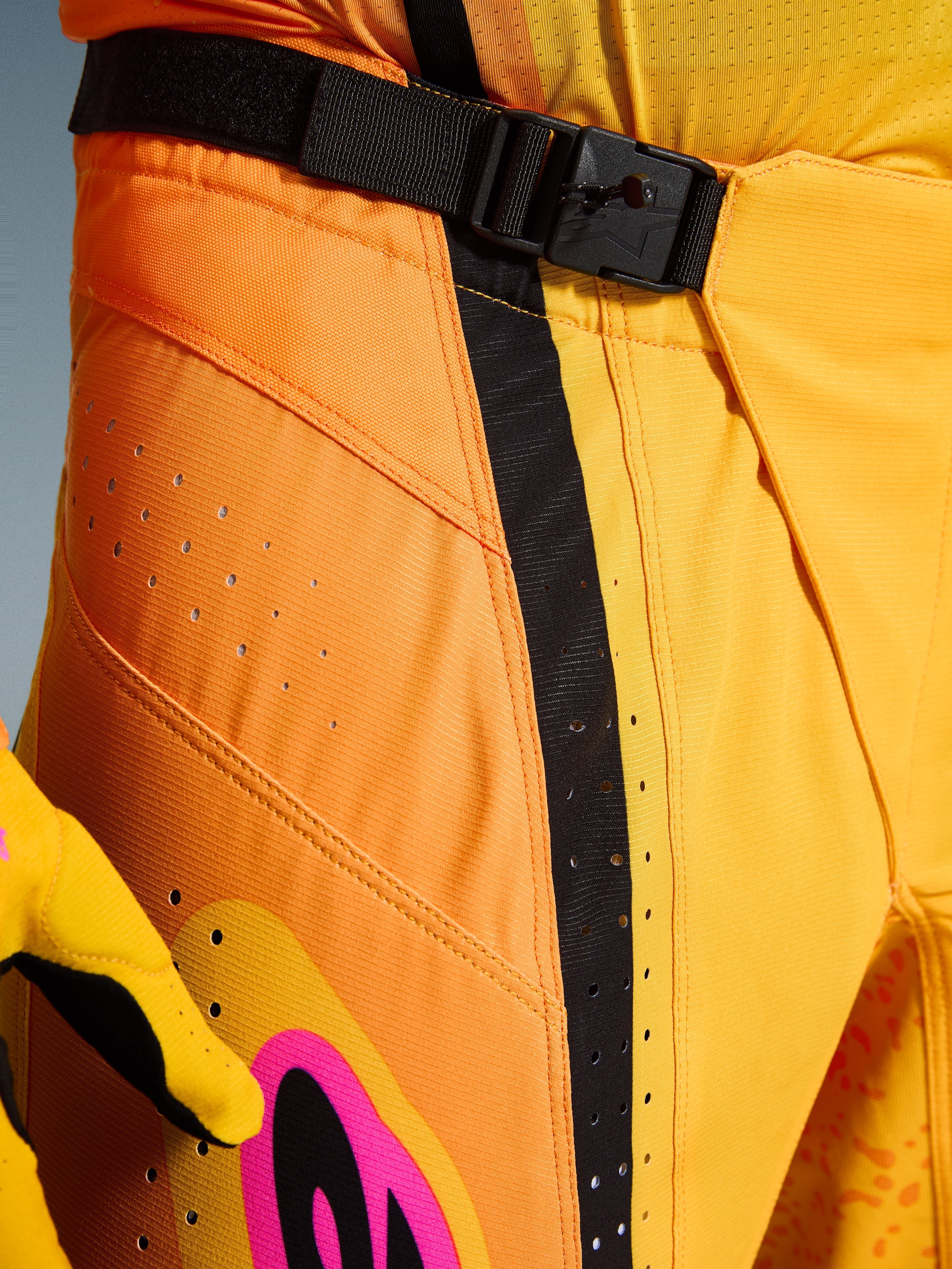 Alpinestars 2026 Techstar Nomur Pants, pantaloni da motocross, arancio giallo rosa, primo piano della zona vita con chiusura magnetica SX2, cinturino di regolazione nero e fori di ventilazione laser su tessuto ripstop resistente