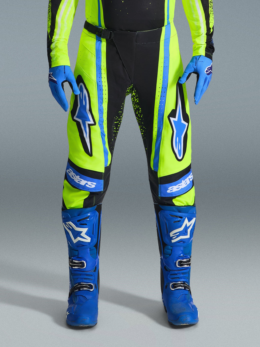 Pantaloni Alpinestars Techstar Nomur 2026, pantaloni da motocross, giallo fluo e blu scuro con accenti blu, indossati con guanti e stivali blu coordinati, caratterizzati da vistosi loghi Astars sulle cosce e un design ad alte prestazioni per il fuoristrada.