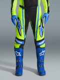 Pantaloni Alpinestars Techstar Nomur 2026, pantaloni da motocross, giallo fluo e blu scuro con accenti blu, indossati con guanti e stivali blu coordinati, caratterizzati da vistosi loghi Astars sulle cosce e un design ad alte prestazioni per il fuoristrada.