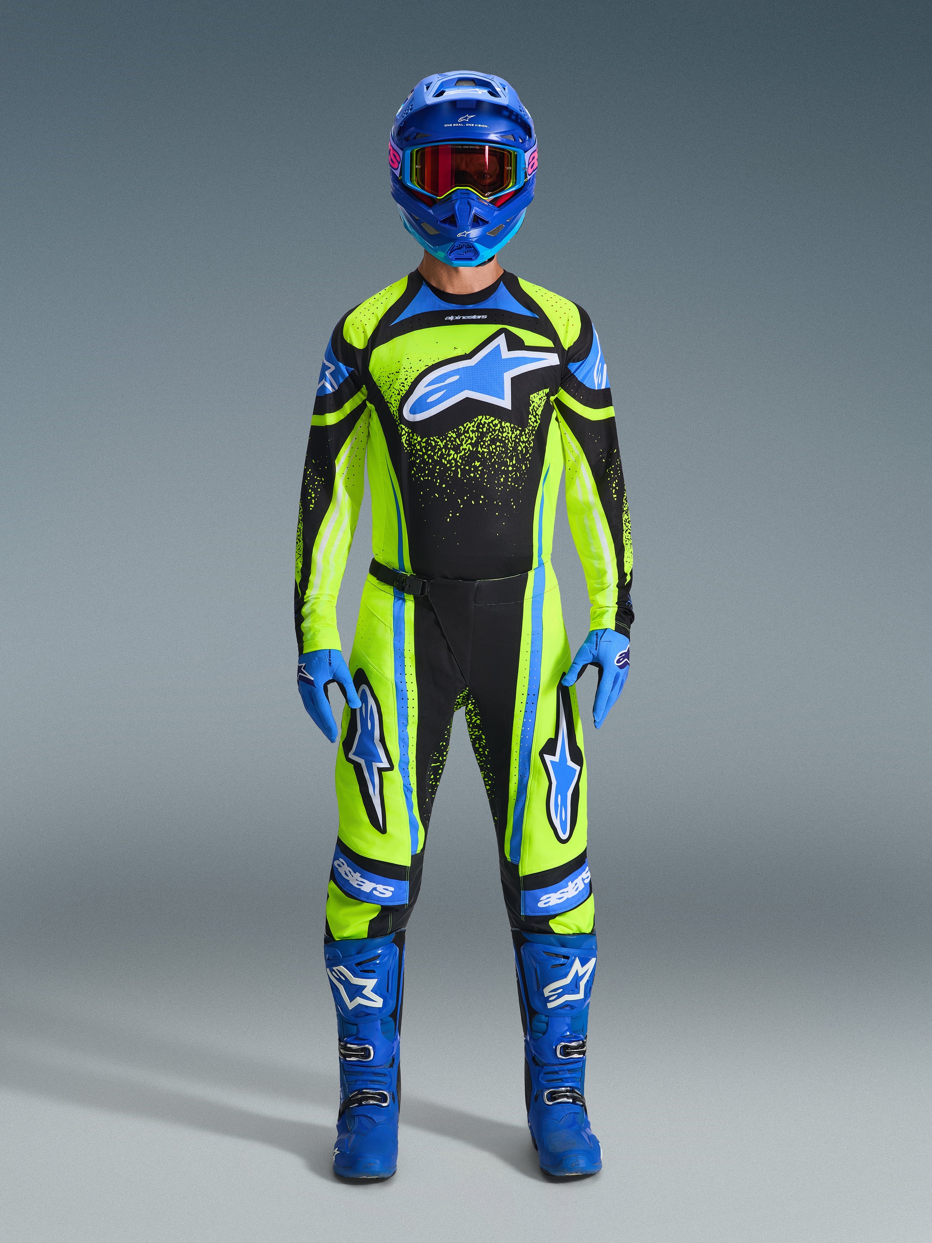 Pilota di motocross con il completo Alpinestars Techstar Nomur 2026, maglia giallo fluorescente e nera con grande logo a stella blu, pantaloni coordinati gialli e neri, casco blu con occhiali, guanti e stivali blu, abbigliamento professionale completo da motocross per corse fuoristrada.