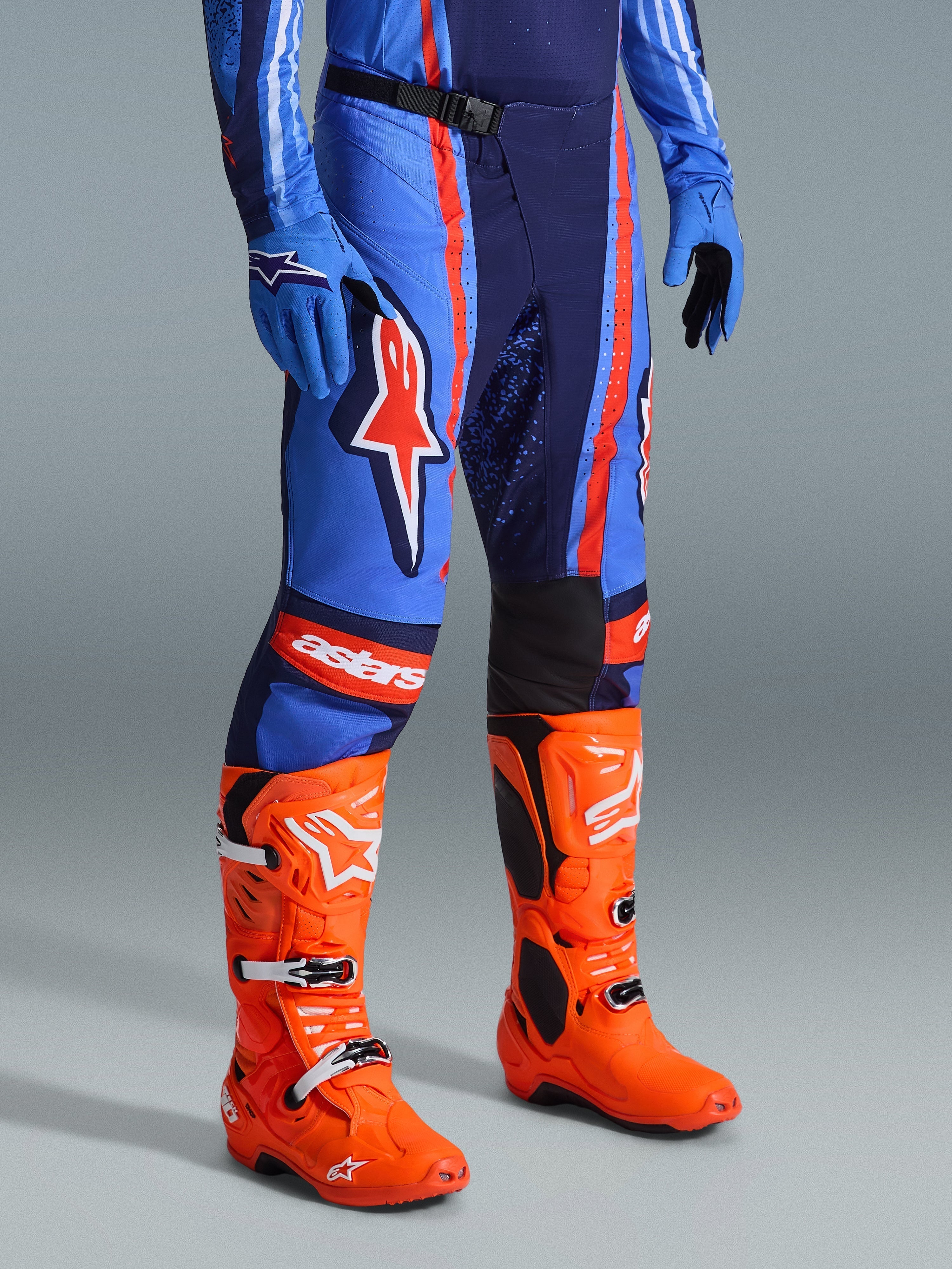 Alpinestars 2026 Techstar Nomur Pants, pantaloni da motocross, blu navy scuro, arancione e blu UCLA, indossati con stivali da motocross arancione brillante e abbigliamento blu coordinato, con loghi evidenti e costruzione multi-materiale per prestazioni fuoristrada.