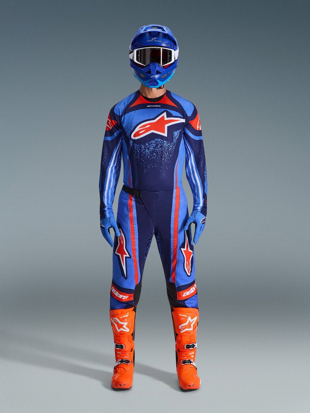 Completo Alpinestars Techstar Nomur 2026, pilota di motocross in kit da gara completo, blu scuro con accenti arancioni e blu UCLA, maglia e pantaloni coordinati con grandi loghi, casco blu e stivali arancione brillante, abbigliamento coordinato per competizioni off-road
