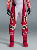 Alpinestars pantaloni Techstar Nomur 2026, pantaloni da motocross, rosso e bianco con accenti neri e gialli, indossati con stivali rossi coordinati e guanti neri, abbigliamento tecnico per gare off-road