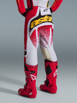 Vista posteriore di un pilota di motocross che indossa i pantaloni Alpinestars Techstar Nomur 2026 in rosso e bianco con un vistoso logo giallo sulla seduta, abbinati a stivali da motocross Tech 10 rosso acceso, scatto in studio su sfondo grigio.