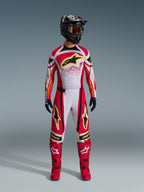 Pilota di motocross che indossa i pantaloni Alpinestars Techstar Nomur 2026, completo da gara off-road rosso, bianco e nero, maglia coordinata con logo stella giallo, casco nero con maschera, stivali rossi e guanti neri, outfit coordinato per il motocross