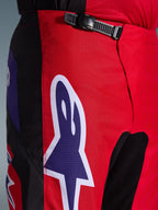 Pantaloni Alpinestars Fluid Grid 2026, pantaloni da motocross, rosso nero e viola, primo piano della zona della vita e dei fianchi con sistema di chiusura a cricchetto nero e grande logo Alpinestars a stella viola con bordo bianco, tessuto strutturato resistente per corse off-road