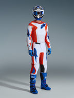 Pilota di motocross che indossa pantaloni Alpinestars 2026 Fluid Grid, arancione e blu UCLA, con base bianca e accenti a stella arancioni e blu, maglia a maniche lunghe coordinata, stivali da motocross blu e casco, abbigliamento da gara professionale completo per prestazioni fuoristrada.