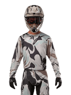 Alpinestars Maglia Racer Tactical 2024, maglia da motocross, motivo mimetico Iron Camo Dust Gray, pilota che indossa casco e occhiali coordinati con guanti neri, abbigliamento tecnico per fuoristrada
