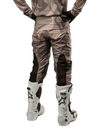 Alpinestars 2024 Racer Tactical Pants, pantaloni da motocross, mimetico verde militare e marrone, vista posteriore che mostra il motivo mimetico e i pannelli elastici neri traspiranti sulla parte inferiore delle gambe, indossati con stivali bianchi da motocross, attrezzatura tecnica resistente per la guida fuoristrada
