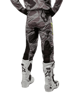 Alpinestars 2024 Racer Tactical Pants, pantaloni da motocross, Cast Gray Camo Magnet, vista posteriore con motivo mimetico e zone elasticizzate traspiranti nere, indossati con stivali da motocross bianchi e neri, progettati per il racing fuoristrada.