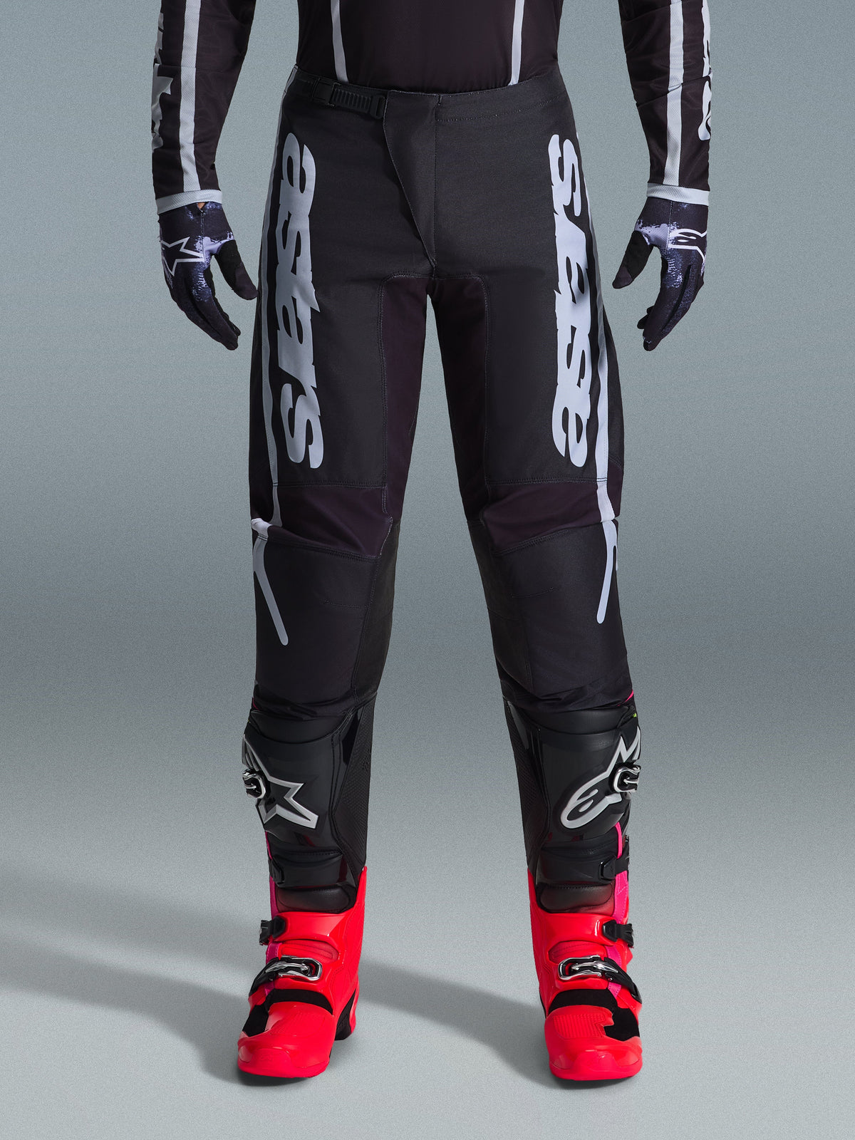Pantaloni Alpinestars 2026 Fluid Apex, pantaloni da motocross neri con grandi scritte bianche, indossati con protezioni per le ginocchia nere e vivaci stivali rossi, telaio leggero in poliestere 600D, design sportivo per gare fuoristrada