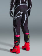 Alpinestars Pantaloni Fluid Apex 2026, pantaloni da motocross, nero e grigio, vista posteriore con grandi loghi Alpinestars bianchi sulla seduta, abbinati a stivali rosso acceso e rosa, costruzione in poliestere 600D per prestazioni off-road