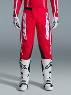 Pantaloni Alpinestars Fluid Apex 2026, pantaloni da motocross, rossi e bianchi, con grandi loghi Astars bianchi sulle cosce e pannelli interni neri sulle ginocchia, indossati con stivali e guanti coordinati bianchi e neri per un look completo da gara off-road.