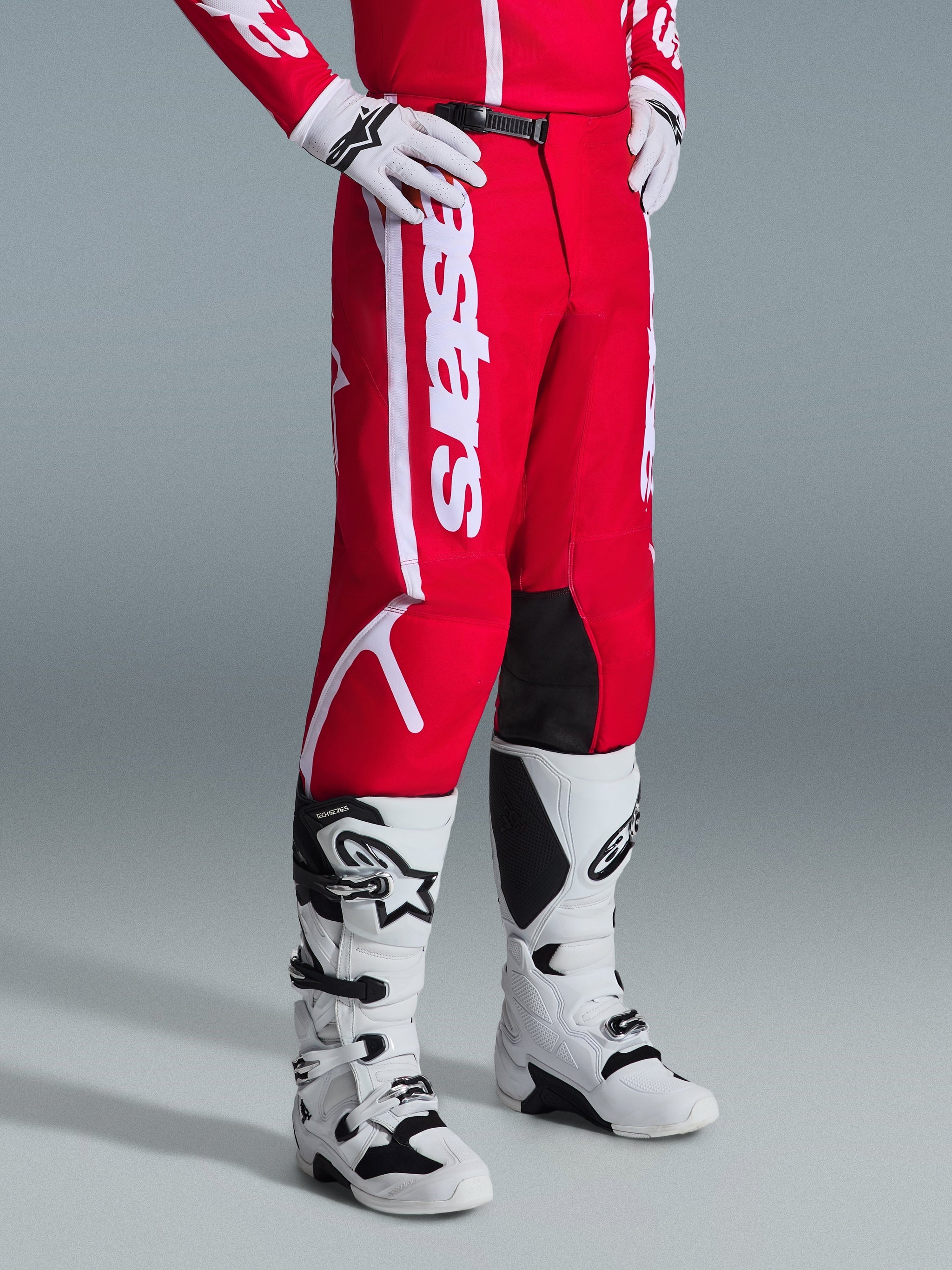 Alpinestars Pantaloni Fluid Apex 2026, pantaloni da motocross, rosso e bianco, indossati con stivali e guanti da motocross bianchi e neri, con logo bianco evidente e inserti neri all'interno del ginocchio, progettati per prestazioni fuoristrada