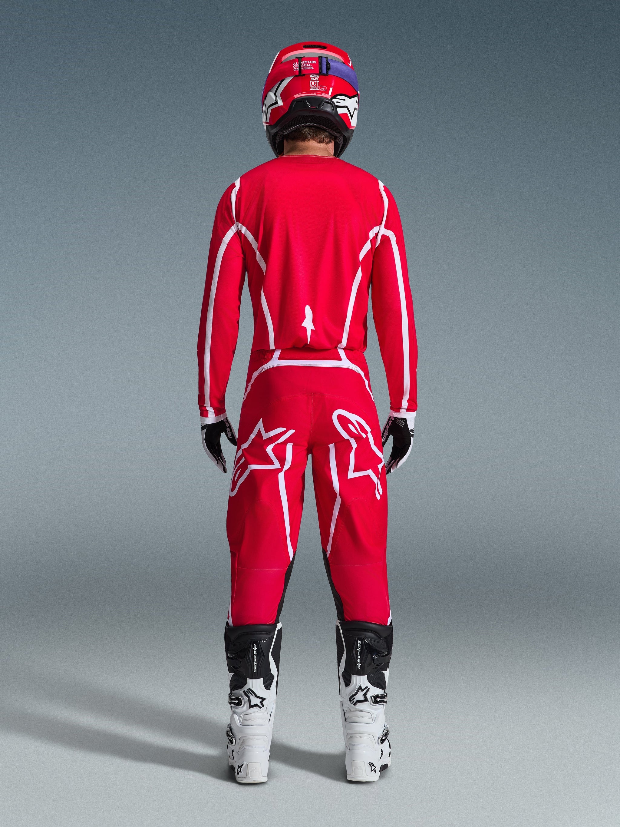 Alpinestars 2026 Fluid Apex Pants, pantaloni da motocross, rosso e bianco, vista posteriore indossati con maglia coordinata, casco rosso e stivali bianchi e neri, con grandi loghi Astar bianchi sulle gambe, outfit coordinato per gare fuoristrada