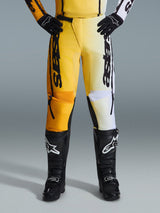 Alpinestars 2026 Fluid Apex Pants, pantaloni da motocross, giallo e nero, design bicolore con pannelli gialli e bianchi, vistoso logo 'astars' verticale, indossati con stivali e guanti da motocross neri, abbigliamento tecnico per guida fuoristrada