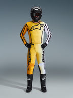 Alpinestars 2026 Fluid Apex Pants, pantaloni da motocross in giallo, nero e bianco, indossati come kit da gara completo con maglia sfumata coordinata, casco nero e stivali, abbigliamento professionale per fuoristrada