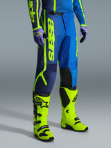 Alpinestars 2026 Fluid Apex Pants, pantaloni da motocross, blu e giallo fluo, indossati con guanti coordinati e stivali giallo fluo vivaci, con branding verticale audace, pannelli rinforzati sulle ginocchia e chiusura a cricchetto in vita.