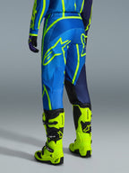 Alpinestars 2026 Fluid Apex Pants, pantaloni da motocross, blu e giallo fluo, vista posteriore del pilota con abbigliamento coordinato e stivali giallo fluorescente, caratterizzati da loghi Alpinestars e design ergonomico