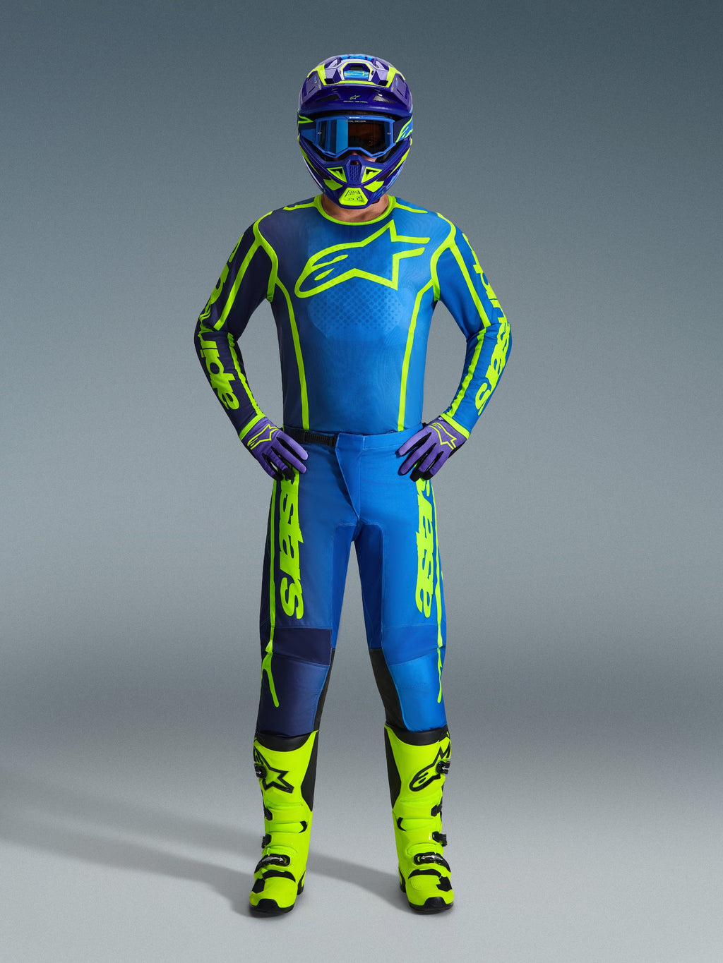 Alpinestars Pantaloni Fluid Apex 2026, pantaloni da motocross, blu e giallo fluo, indossati da un pilota con maglia, casco, guanti e stivali coordinati, con vistoso logo Alpinestars giallo su base blu, completo da gara fuoristrada coordinato