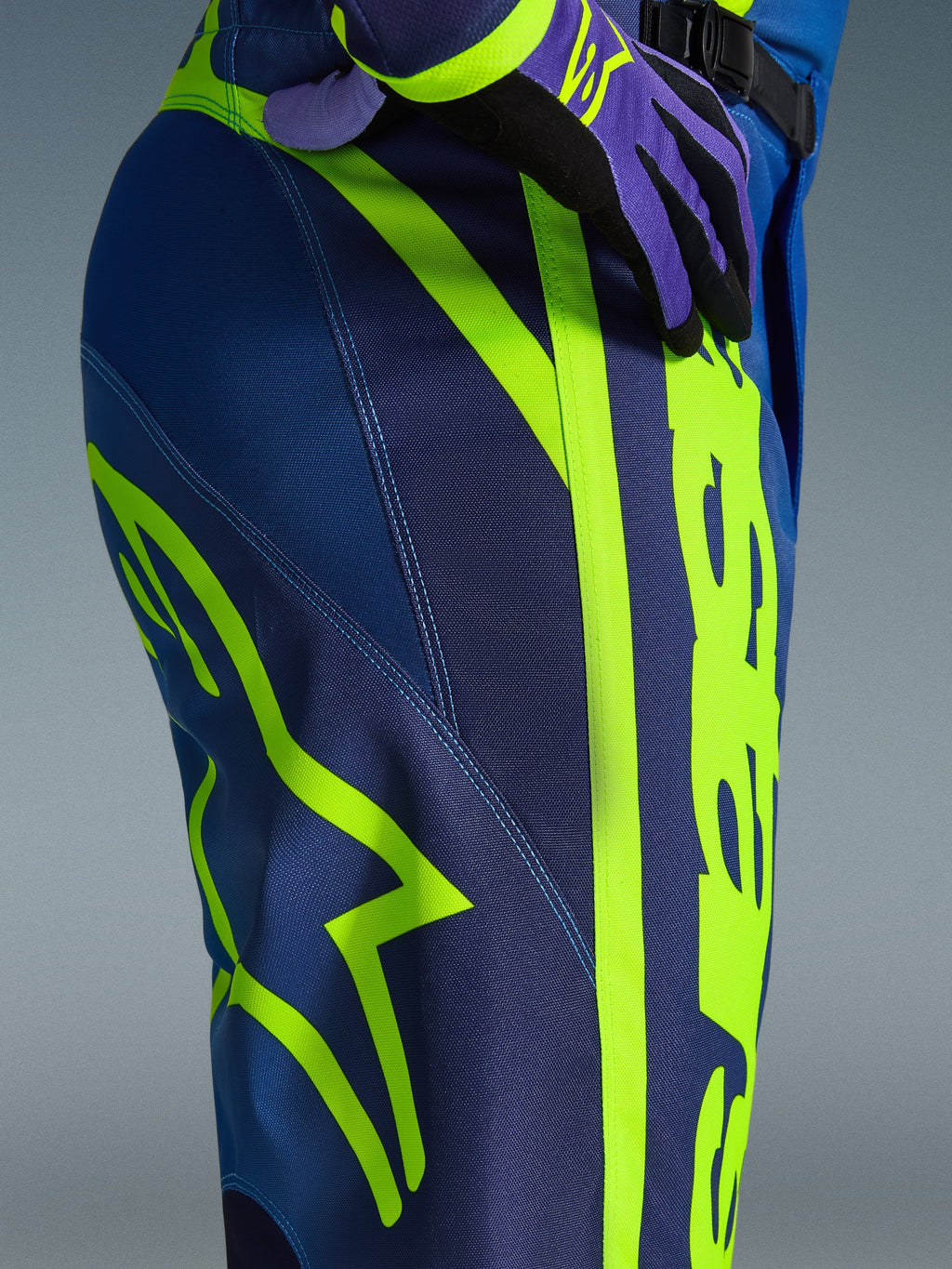 Alpinestars Pantaloni Fluid Apex 2026, pantaloni da motocross, blu e giallo fluo, vista ravvicinata del fianco con vistoso logo Alpinestars giallo neon, resistente materiale in poliestere per guida fuoristrada, parte di un completo coordinato