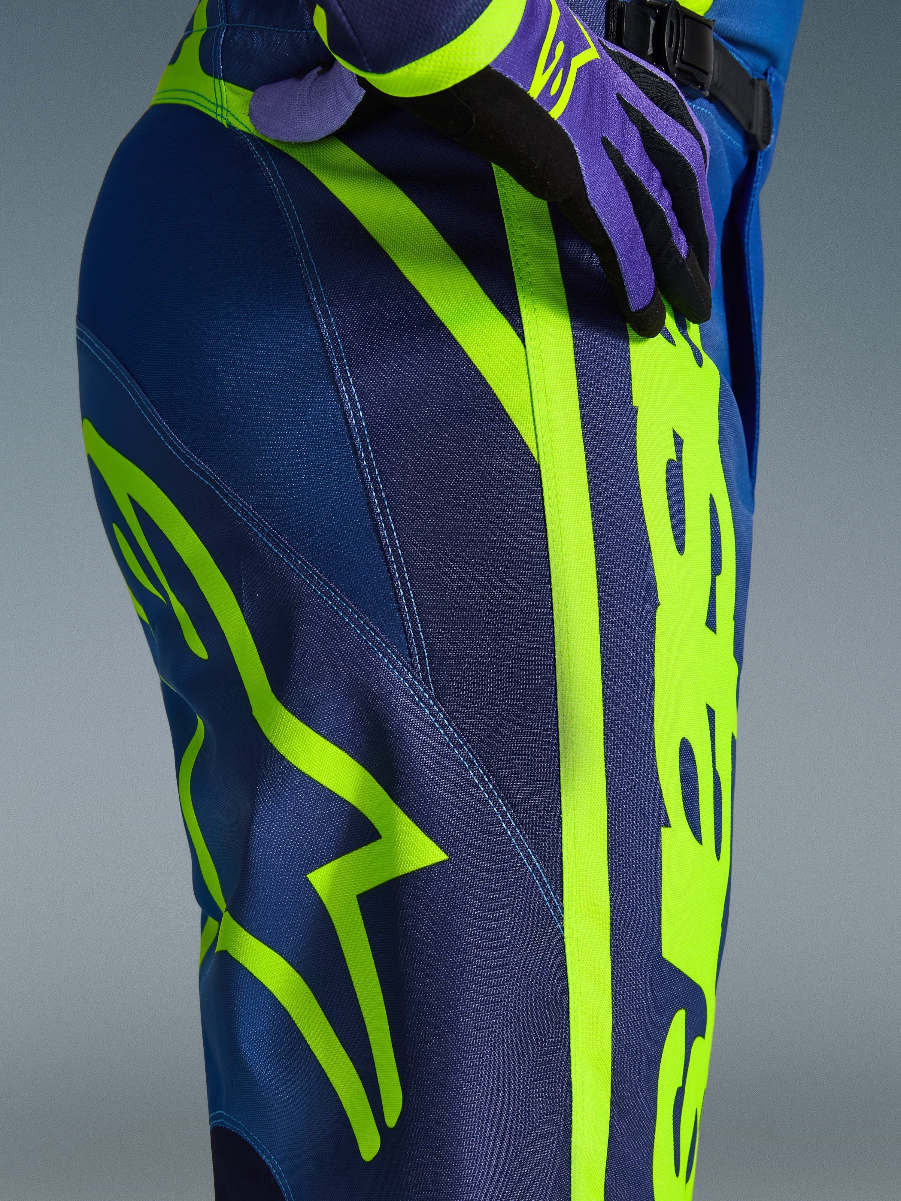Alpinestars Pantaloni Fluid Apex 2026, pantaloni da motocross, blu e giallo fluo, vista ravvicinata del fianco con vistoso logo Alpinestars giallo neon, resistente materiale in poliestere per guida fuoristrada, parte di un completo coordinato